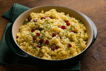 Couscous with pomegranate seeds on wooden background