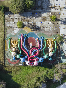 Aerial view of a vibrant playground with colorful octopus-like structures standing out against the weathered concrete, surrounded by green grass, Battipaglia, Campania, Italy.