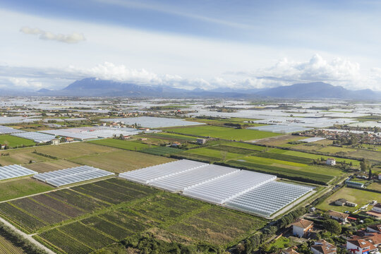 Aerial view of vast agricultural fields and greenhouses creating a patchwork quilt across the landscape, framed by distant mountains, Battipaglia, Campania, Italy.