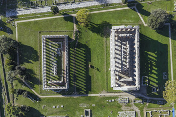 Aerial view of the ancient Greek temples stand majestically, their weathered stones contrasting against the vibrant green of the surrounding fields, Paestum, Campania, Italy.