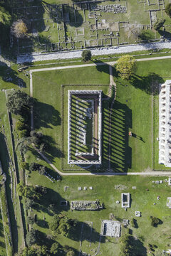 Aerial view of ancient ruins bathed in sunlight casting long shadows across the verdant grass of Paestum, Campania, Italy.