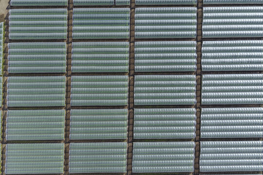 Aerial view of a grid of greenhouses stretch across the landscape, their metallic surfaces reflecting the sky, creating a shimmering pattern, Paestum, Campania, Italy.