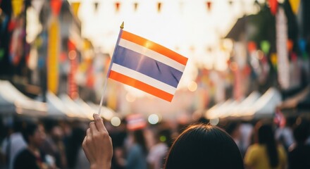 Hand Waving Small Thailand Flag at Vibrant, Sun-Drenched Street Festival