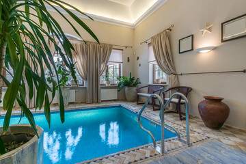 A small indoor swimming area is visible with bright water. Plants are placed around the pool. There...