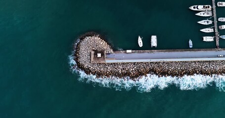 Aerial view of the pier with boats anchored contrasts with the crashing waves against the rock barrier, Agropoli, Campania, Italy.