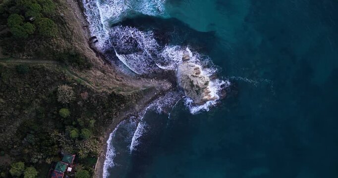 Aerial view of the rugged coastline meeting the turquoise sea, with a sea stack standing firm against crashing waves, Agropoli, Campania, Italy.