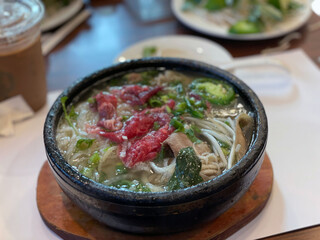 traditional Vietnamese noodles (Pho Dac Biet) served in a traditional stone bowl, featuring a flavorful mix of beef, meatballs, herbs, and vermicelli noodles.