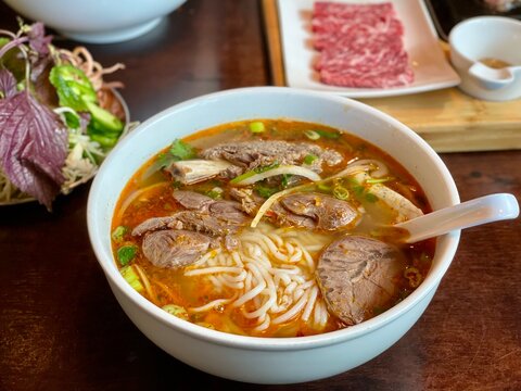 Authentic Vietnamese noodle soup B&uacute;n B&ograve; Huế featuring beef, rice noodles, chili broth, and fresh herbs