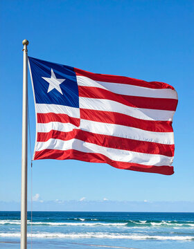 A detailed shot of the distinct, colorful Liberian flag waving gently against a bright, clear blue coastal sky.