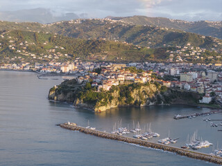 Aerial view of the old town perched on a dramatic rocky outcrop, contrasting with the calm, reflective sea and the distant, verdant hills, Agropoli, Campania, Italy.