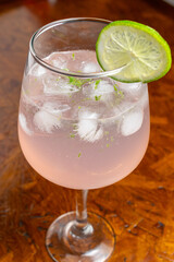 Pink Gin Tonic Spritz cocktail with a slice of lime and ice in a balloon glass on a rustic wooden table