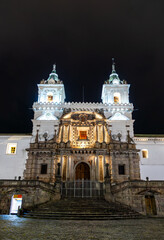 Church of San Francisco stands on cobblestone plaza in Quito, Ecuador. Historic colonial complex features twin towers and stone facade in UNESCO World Heritage center under night sky