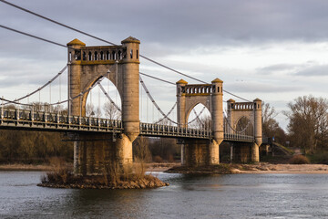 Obraz premium Historic Suspension Bridge Over Calm River at Sunset