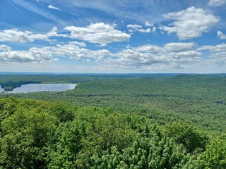 Obraz premium A bird's eye view of the Adirondack landscape below a mountain top fire tower overlooking wilderness, lakes and dramatic blue skies and white clouds.
