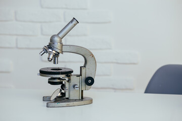 an old iron microscope is on the desktop in the office. equipment for studying microbes, viruses, biological samples of plants and humans. concept: studying epidemics and pandemics