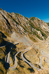 Sharp road curves of Transfagarasan Highway weaving through sunlit mountain landscape. Fagaras mountains, Romania. Travel concept.