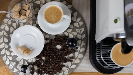 Top view of two coffee cups on saucers with coffee, sugar bowl and coffee machine on wooden table