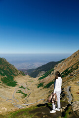 Back view of young woman standing on cliff edge with panoramic mountain landscape of Transfagarasan Highway, Romania. Travel concept