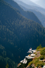 Young woman sitting on cliff edge above deep forest valley in Fagaras Mountains, Romania. Transfagarasan Highway. Freedom, solo travel, mindfulness concept.