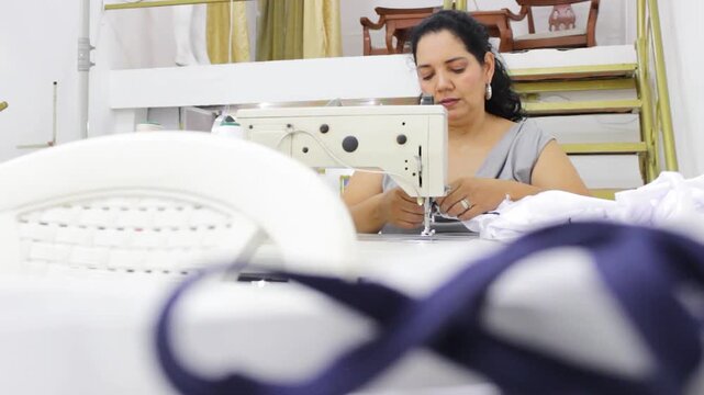 A Colombian woman is working on a sewing machine to create a new clothing collection line inside an industrial workshop in Neiva, Huila, Colombia. Concept of textile industry 