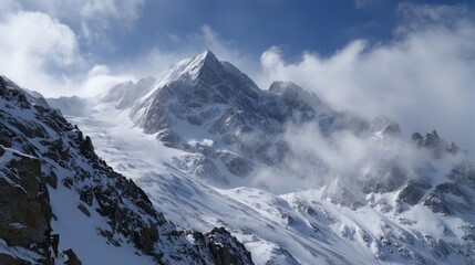Obraz premium A high mountain covered in snow rises above clouds with a rocky area in the foreground. The sky is mostly clear with some clouds scattered. Bright daylight shines on the scene.