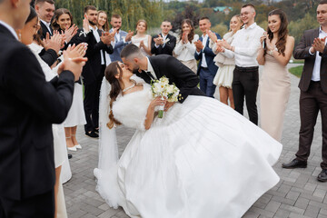 Couple shares a romantic kiss surrounded by friends during outdoor wedding celebration