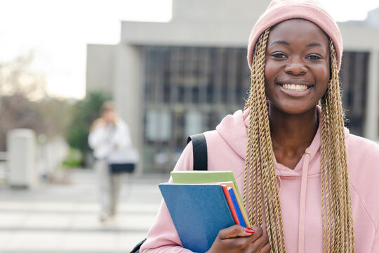 African American female student standing on campus holding textbooks with backpack, copy space