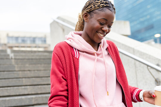 African American woman standing on plaza stairs holding coffee cup near handrail, copy space