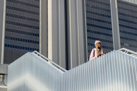 African American woman standing on staircase by railing holding phone with backpack, copy space