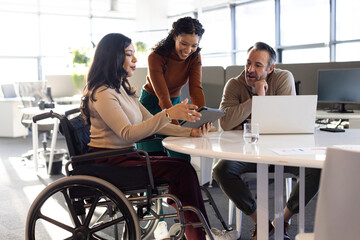 Diverse coworkers collaborating around round table in modern office using tablet and laptop