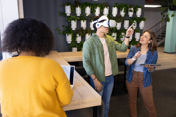 Diverse coworkers collaborating at table in office using laptop, VR headset and tablet, copy space