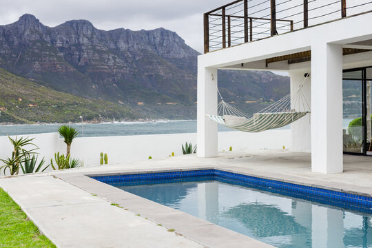 Striped hammock hanging from pergola posts above pool deck with cacti overlooking sea and mountains