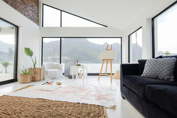 Naklejka premium Wooden easel standing on drop cloth with brushes and paints in loft overlooking lake and mountain