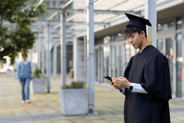 Diverse classmates standing on campus walkway wearing mortarboard and using smartphone, copy space