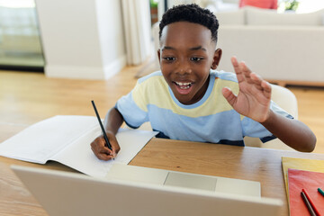 African American boy holding pencil, raising hand at home desk with laptop notebook red folder