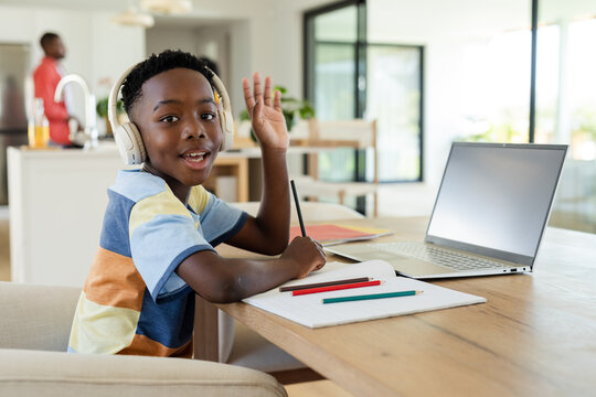 African American father supervising son studying at table in open plan kitchen with laptop
