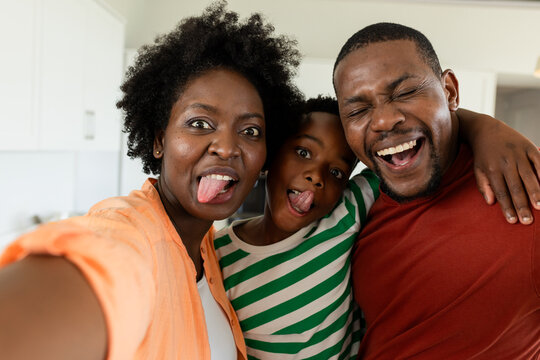 African American family taking selfie in home kitchen using smartphone and sticking tongues out