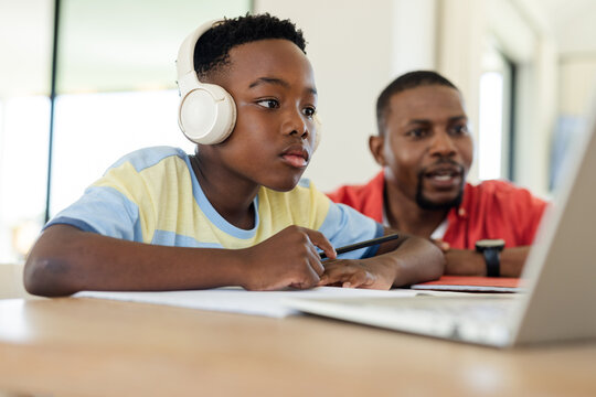 African American father and son studying using stylus and laptop at study table wearing headphones