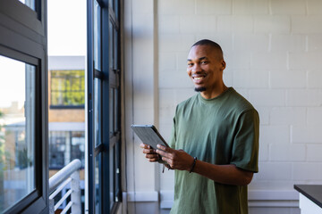 African American man wearing green t-shirt standing in office by multipane window holding tablet