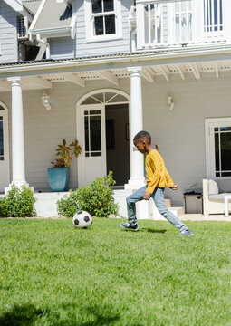 Child is kicking black-and-white soccer ball on green lawn in front of light-gray house