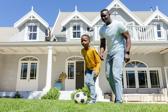 African American father and child standing on well-kept lawn in front of house, soccer ball
