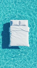 A pristine white bed with two pillows and a duvet floats peacefully on shimmering turquoise blue water under bright sunlight, viewed from directly above.
