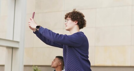 Diverse male friends standing in plaza, one raising smartphone for selfie after other glancing up - Powered by Adobe