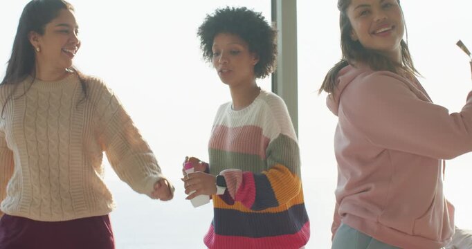 Diverse female friends shaking bottle grabbing snack bar and dancing for morning boost at window
