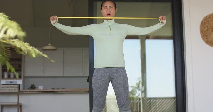 Starting warm-up with resistance band pull-aparts, Asian woman strengthening shoulders on patio