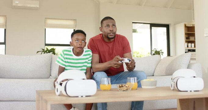 African American father and son sitting on sofa, grabbing controller and playing game for bonding