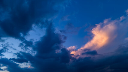 Obraz premium Moody sky composition showing dark blue storm clouds contrasting with a patch of golden sunlight reflecting off a cumulus formation indicating the transition between storm and sunset