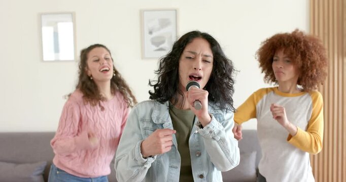 Diverse female friends starting karaoke with remote, grabbing mic and singing verse in living room
