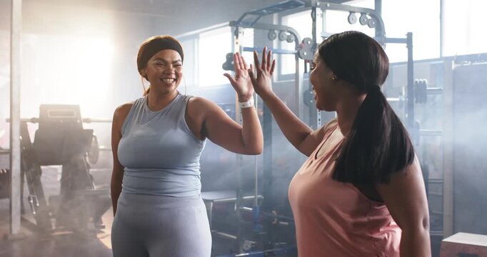 Two mid-adult women sharing high-five celebrating workout success in gym by cable machine