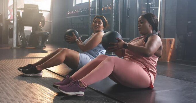 Diverse female partners gripping medicine ball and twisting torso in gym building core strength